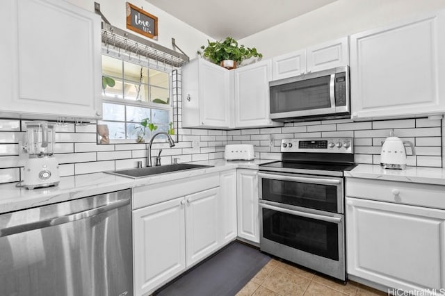 kitchen featuring light stone counters, stainless steel appliances, sink, light tile patterned floors, and white cabinets