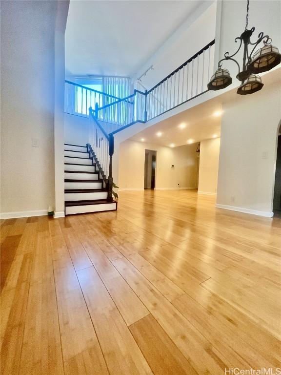 unfurnished living room with a high ceiling, a chandelier, and light hardwood / wood-style floors