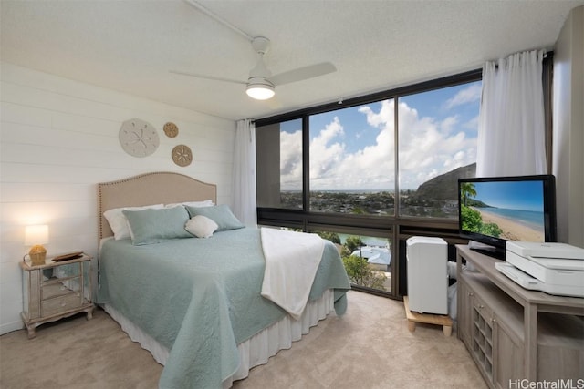 carpeted bedroom featuring ceiling fan, a wall of windows, and a textured ceiling