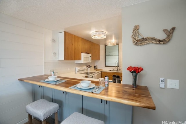 kitchen with a textured ceiling, white appliances, sink, and a breakfast bar area