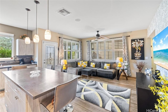 kitchen with light hardwood / wood-style flooring, ceiling fan, light brown cabinetry, a kitchen island, and a breakfast bar area