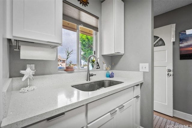 kitchen featuring light stone countertops, hardwood / wood-style floors, white cabinetry, and sink