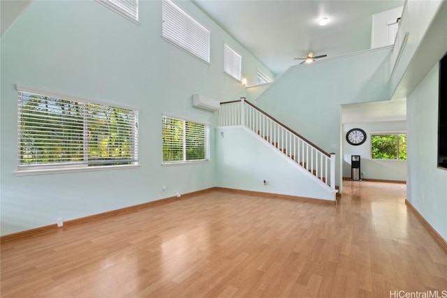 unfurnished living room featuring a high ceiling, light hardwood / wood-style flooring, ceiling fan, and a wall unit AC