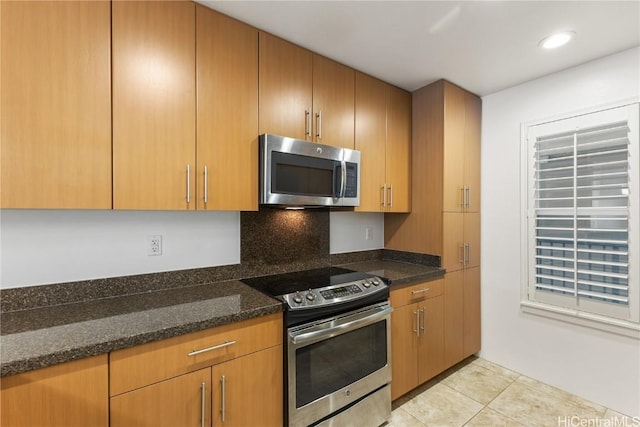 kitchen featuring dark stone counters, appliances with stainless steel finishes, light tile patterned flooring, and recessed lighting