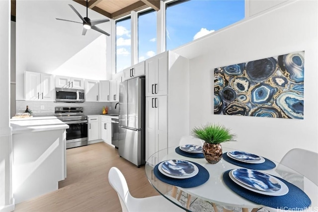 kitchen featuring tasteful backsplash, light hardwood / wood-style floors, a high ceiling, white cabinetry, and stainless steel appliances