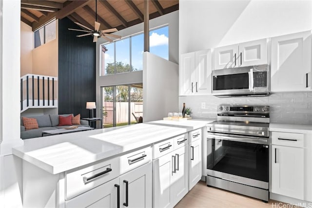 kitchen with white cabinetry, stainless steel appliances, decorative backsplash, high vaulted ceiling, and beam ceiling