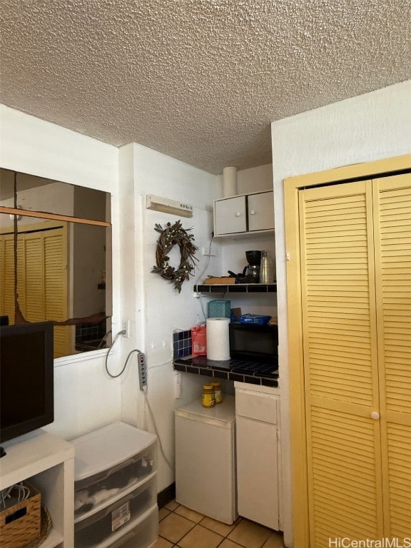 kitchen featuring white cabinetry, tile counters, light tile patterned floors, and a textured ceiling