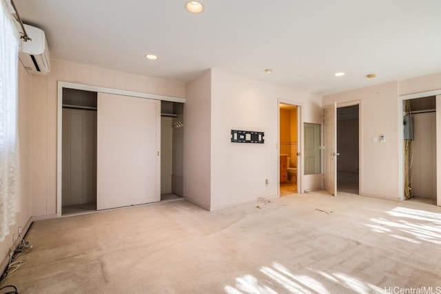 unfurnished bedroom featuring light colored carpet, ensuite bath, and a wall mounted AC