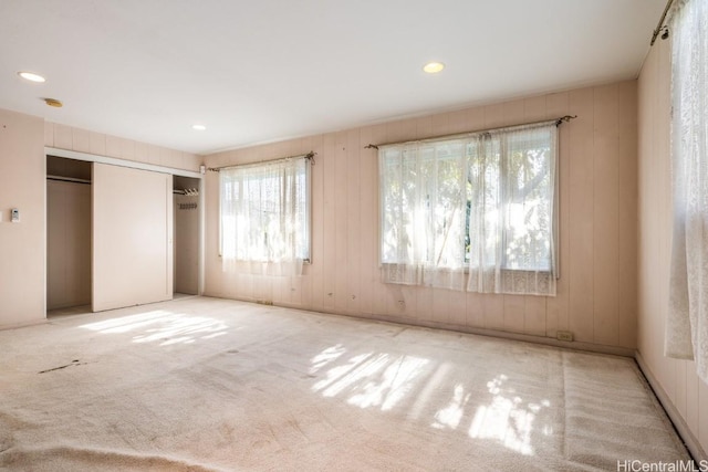 unfurnished bedroom featuring wood walls, a closet, and light colored carpet