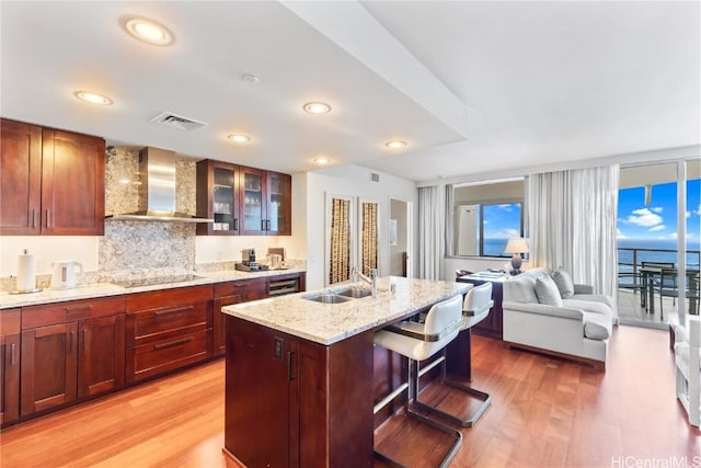 kitchen with black electric stovetop, a kitchen island with sink, sink, wall chimney range hood, and a water view