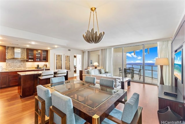 dining space featuring floor to ceiling windows, a chandelier, a water view, and light hardwood / wood-style floors