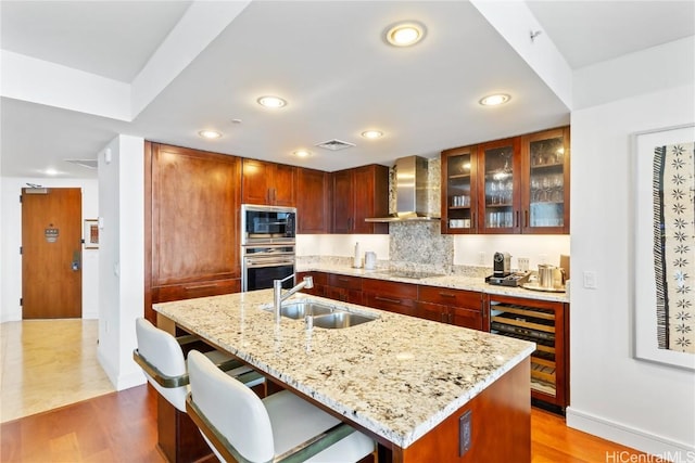 kitchen featuring a center island with sink, oven, wall chimney range hood, and sink