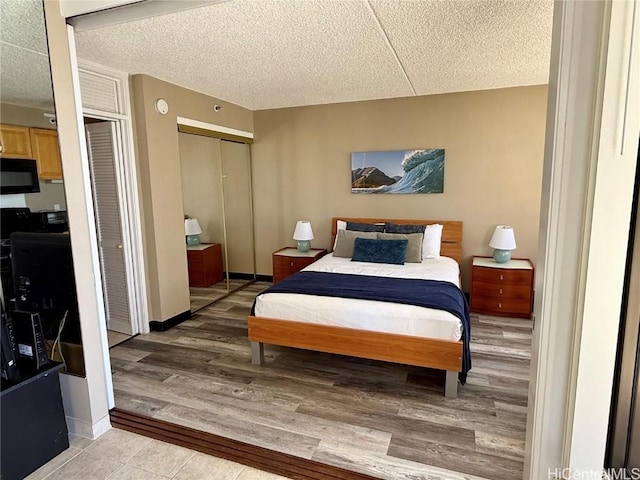 bedroom with multiple closets, light wood-style flooring, baseboards, and a textured ceiling