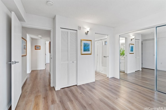 unfurnished bedroom featuring ensuite bath, two closets, a textured ceiling, and light wood-type flooring