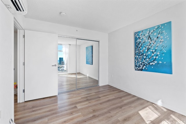 unfurnished room with a textured ceiling, light hardwood / wood-style flooring, and a wall unit AC