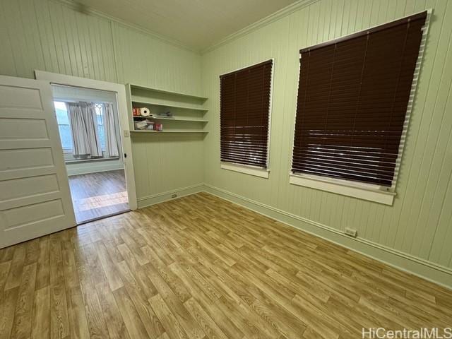 unfurnished room featuring wooden walls, light hardwood / wood-style floors, and ornamental molding