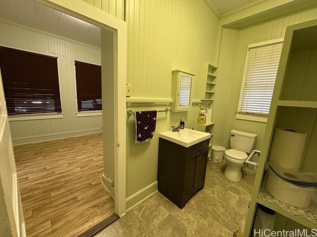 bathroom featuring vanity, wood walls, built in shelves, toilet, and ornamental molding