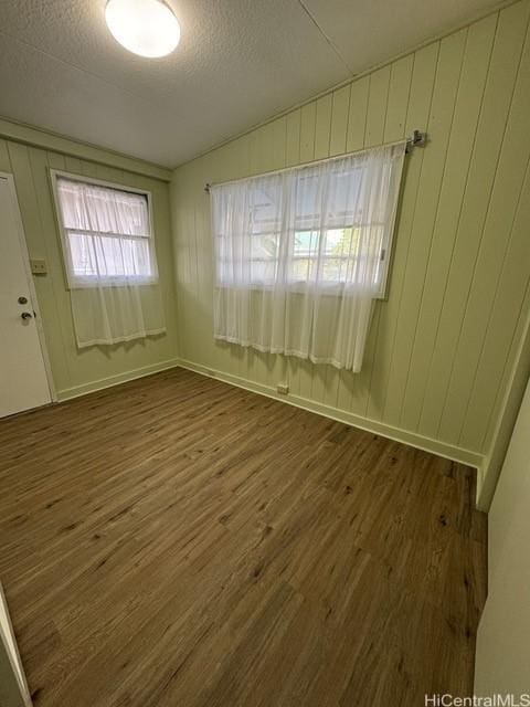 empty room with a textured ceiling, wood walls, vaulted ceiling, and dark hardwood / wood-style floors