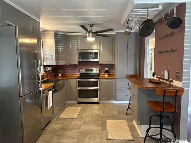 kitchen with appliances with stainless steel finishes, wooden counters, gray cabinets, and sink