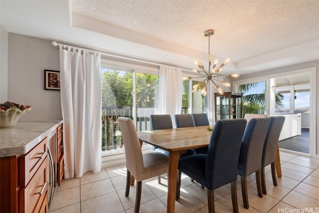 tiled dining room featuring a notable chandelier, a raised ceiling, and a textured ceiling