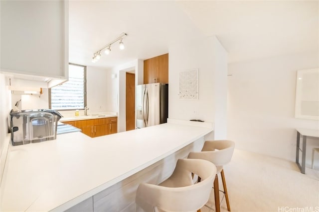 kitchen featuring sink, stainless steel fridge, light colored carpet, kitchen peninsula, and a breakfast bar area