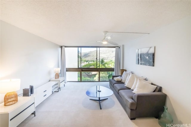 living room featuring ceiling fan, light carpet, a textured ceiling, and a wall of windows