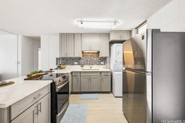 kitchen with appliances with stainless steel finishes, stacked washing maching and dryer, gray cabinetry, a textured ceiling, and sink