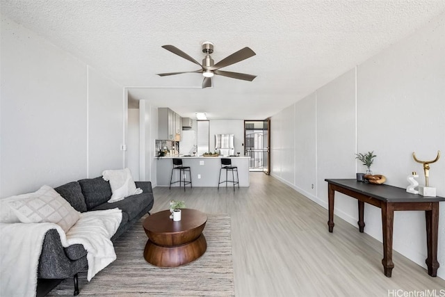 living room with ceiling fan, light hardwood / wood-style floors, and a textured ceiling