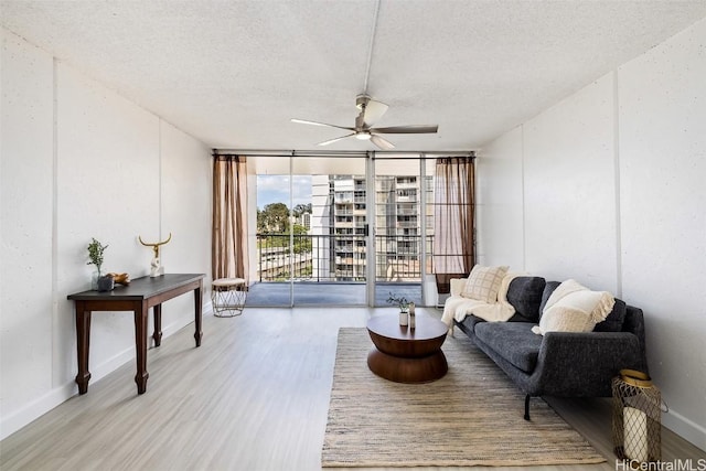 living room featuring ceiling fan, light wood-type flooring, a wall of windows, and a textured ceiling