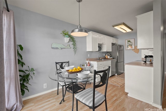 kitchen featuring appliances with stainless steel finishes, pendant lighting, white cabinetry, sink, and light hardwood / wood-style floors