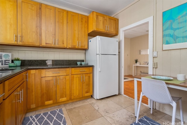 kitchen with dark stone countertops, sink, and white fridge