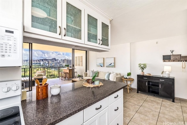 kitchen featuring white cabinets, light tile patterned flooring, dark stone countertops, and white range