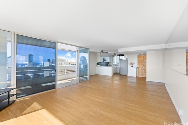 living area with a city view, floor to ceiling windows, light wood-type flooring, and ceiling fan