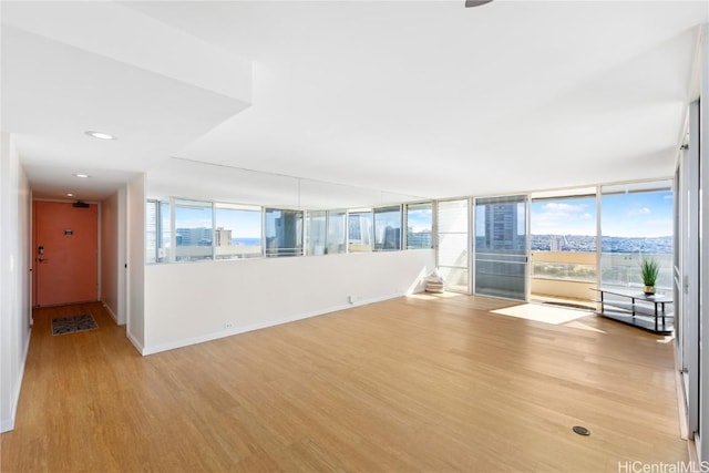 unfurnished room featuring a view of city, recessed lighting, baseboards, and light wood-type flooring