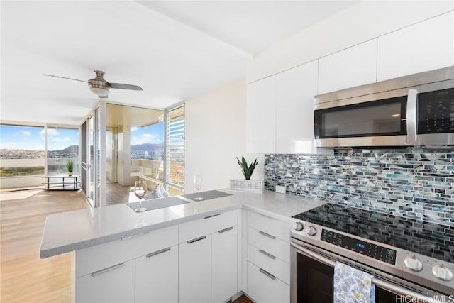 kitchen with white cabinetry, tasteful backsplash, kitchen peninsula, appliances with stainless steel finishes, and light wood-type flooring