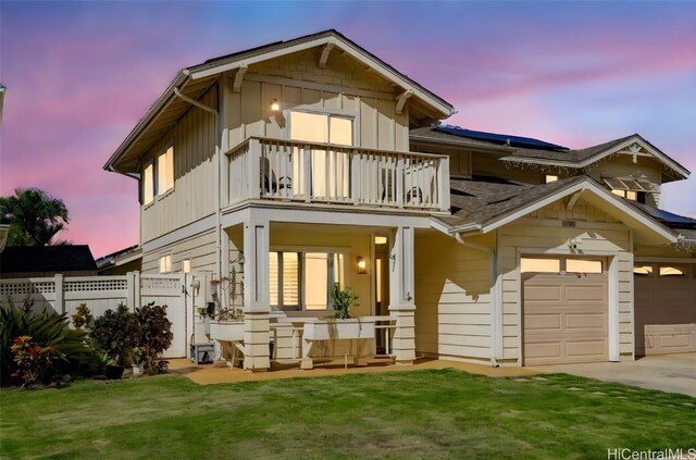 back house at dusk featuring a lawn, a garage, and a balcony