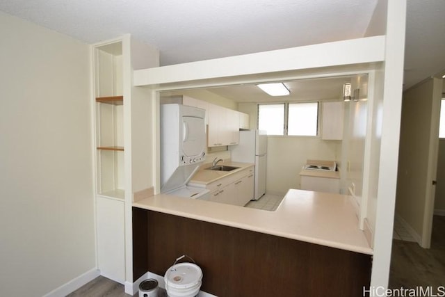 kitchen with kitchen peninsula, white refrigerator, light hardwood / wood-style flooring, white cabinetry, and stacked washer / drying machine