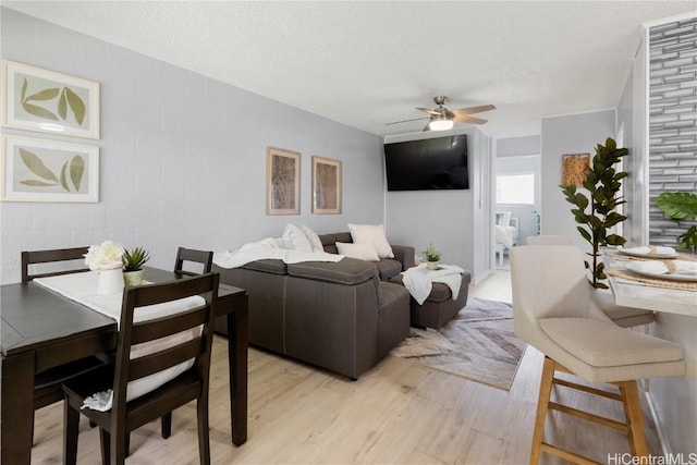 living room with ceiling fan, a textured ceiling, and light hardwood / wood-style floors