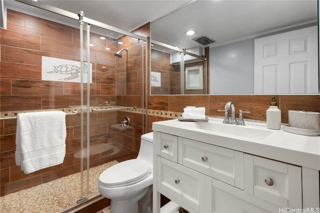 bathroom with toilet, tile walls, vanity, a shower with door, and backsplash