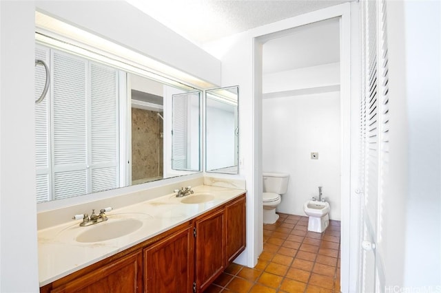 bathroom with vanity, toilet, a textured ceiling, and a bidet