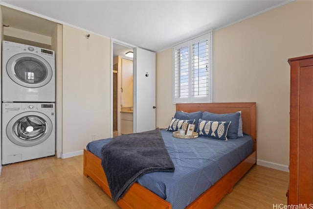 bedroom featuring stacked washing maching and dryer, light wood-type flooring, and baseboards