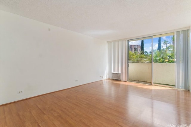 empty room with a wall of windows, a textured ceiling, and light wood-type flooring