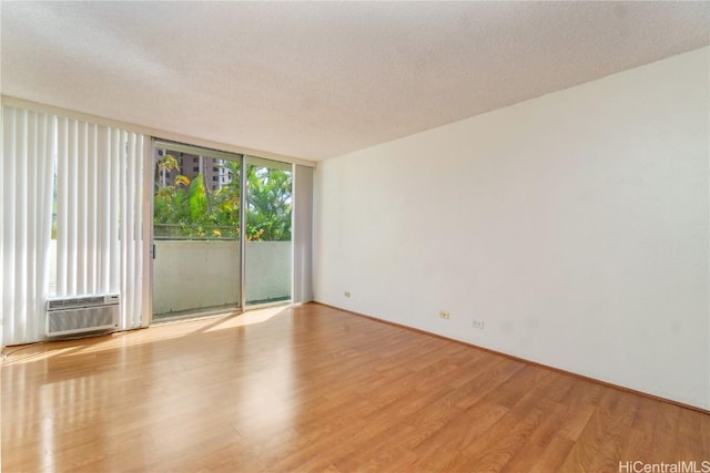 empty room featuring a wall unit AC, a wall of windows, a textured ceiling, and light hardwood / wood-style flooring