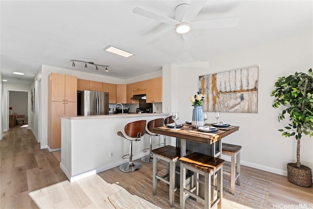 kitchen featuring light brown cabinetry, light hardwood / wood-style floors, kitchen peninsula, stainless steel refrigerator, and ceiling fan