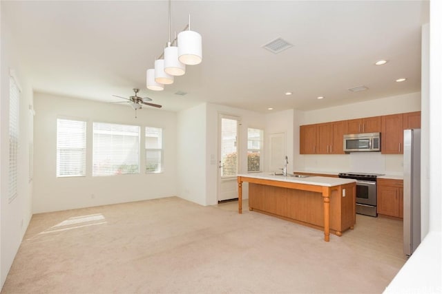 kitchen featuring a center island with sink, sink, hanging light fixtures, ceiling fan, and stainless steel appliances