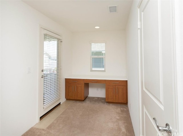 unfurnished office with a healthy amount of sunlight, light colored carpet, and built in desk