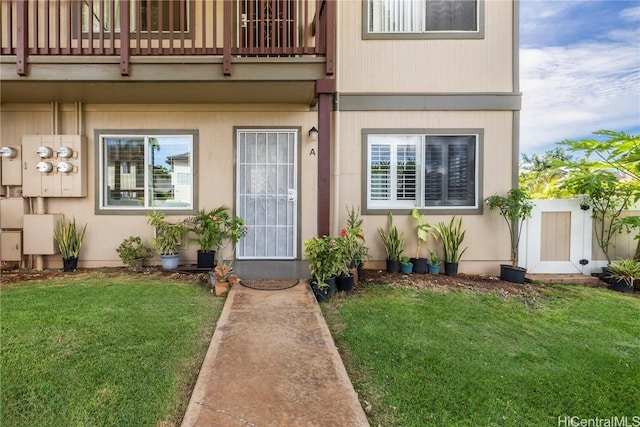 view of exterior entry with a balcony and a lawn