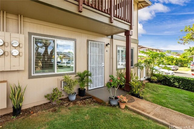 view of exterior entry with a balcony and a yard