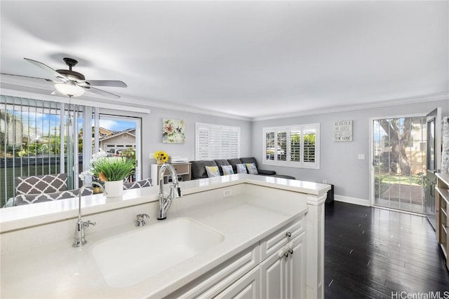 kitchen featuring a sink, white cabinets, light countertops, dark wood finished floors, and crown molding