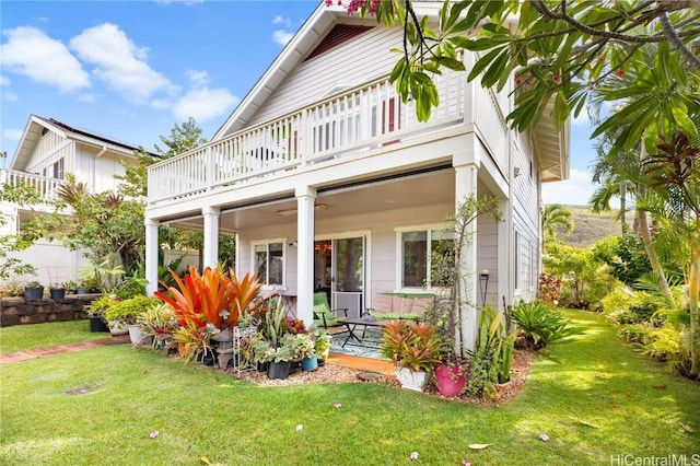 rear view of house with ceiling fan, a balcony, and a yard